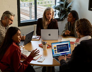 Un grupo de cinco empleados sentados en una mesa en una sala de reuniones, durante la reunión usan tres MacBook Pro.